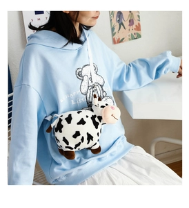 Detail view of light blue hoodie featuring a 3D plush cow toy and Be Happy Bear graphics