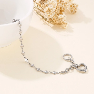 Silver stainless steel heart link bracelet with T-bar toggle clasp draped over a white ceramic bowl