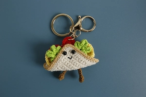 Detailed top view of a handmade crochet taco keychain with metal ring on blue background