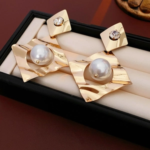 Close-up of geometric gold earrings with waves and pearls on a premium jewelry box