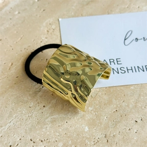 Detail of golden metal hair tie with irregular wavy texture and black elastic band