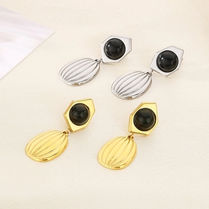 Detailed view of gold and silver teardrop earrings with black bead on textured surface