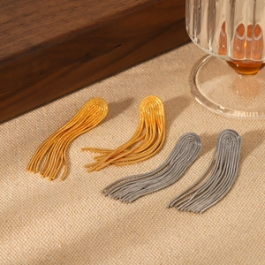 Detail shot of long tassel chain earrings in gold and silver finish on textured background