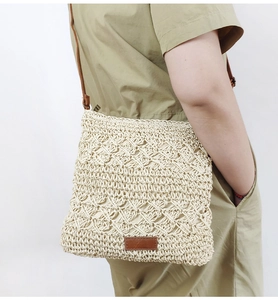 Detailed close-up of hollowed-out paper rope weave texture and brown leather strap on bag