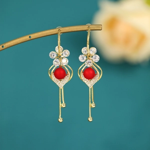 Detail of vintage gold earrings with red beads and long tassels on a green backdrop