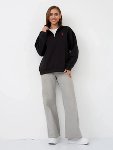 Detail of black half-zip sweatshirt with small red heart logo and grey wide-leg denim jeans