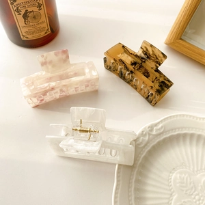 Three acetate hair claw clips in pearl white, pink stone, and tortoiseshell patterns