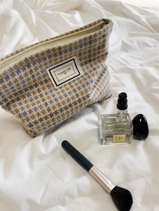 Detail of tweed checkered makeup bag with PLEASANT TIME label on white bedding