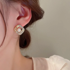 Primo piano dell'orecchino quadrato dorato con perla e strass sull'orecchio della modella