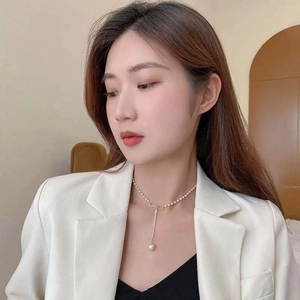 Detailed view of gold bow necklace featuring long elegant dangling white pearl pendant