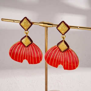 Detail of red enamel fish tail earrings with golden diamond texture on a metal stand