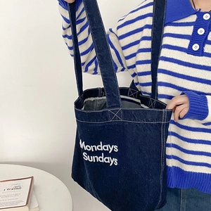 Sac fourre-tout en denim bleu foncé avec broderie blanche porté par un mannequin en pull rayé