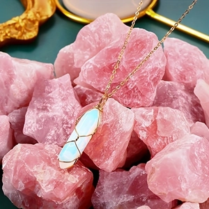 Detail of opal hexagonal crystal pendant with gold wire wrap on pink stone background