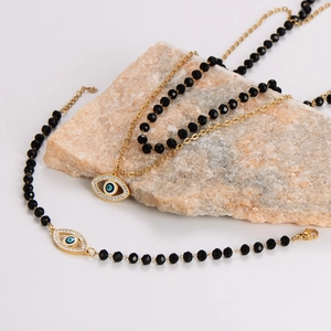 Golden Evil Eye jewelry set with black glass beads and necklace on stone background