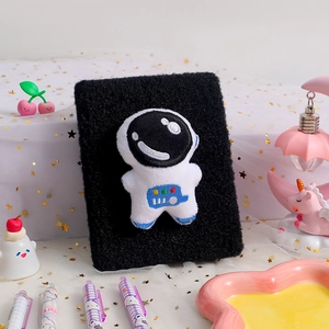 Close-up of black plush notebook featuring a cute white astronaut embroidery decoration