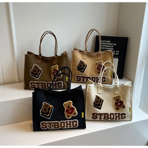 Detail of four colorful canvas tote bags featuring plush bear patches and embroidery