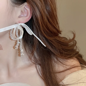 Close-up of elegant white ribbon bow earrings with transparent beads on a female model