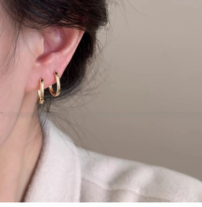 Primo piano di orecchini a cerchio ovali placcati oro 18 carati indossati da una modella