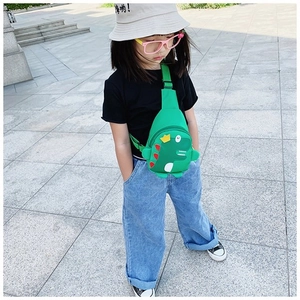 Close-up of a green cartoon dinosaur chest bag for kids with adjustable strap outdoors