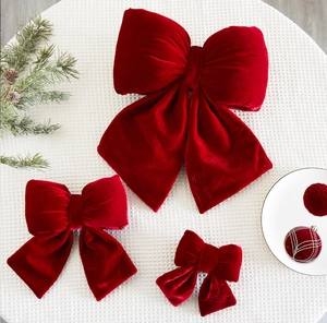 Three sizes of burgundy velvet Christmas bows arranged with pine cones on white cloth