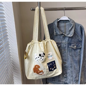 Detail of off-white canvas tote bag with cartoon animal embroidery hanging on a metal rack