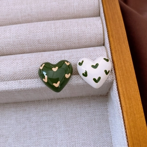 Detailed shot of two heart-shaped enamel earrings in beige jewelry box with wooden frame
