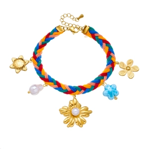 Close-up of woven colorful bracelet featuring gold floral charms and pearl details