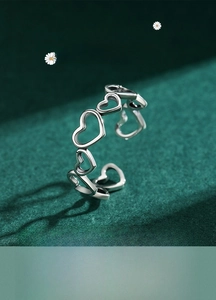 Macro shot of silver S925 hollow heart ring with adjustable open band on green background