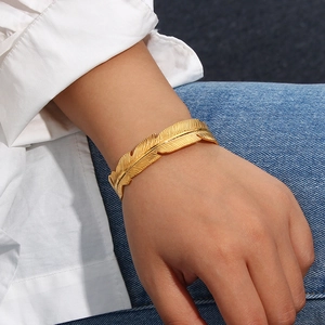 Detail of 18K gold-plated feather open cuff bracelet with brushed metal texture on wrist