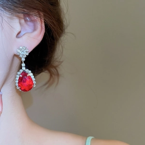 Dettaglio orecchini a goccia rossi con accenti floreali su base in argento lucido