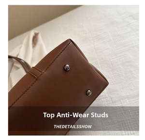 Detailed macro view of metal protective feet on a dark brown textured leather tote bag