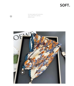 Detail of floral pleated scarf with magnetic buckle and decorative tassel on black tray