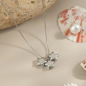 Close-up of a silver necklace with three star pendants on a natural rock background