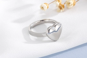 Gros plan d'une bague coeur en argent poli sur tissu blanc au style minimaliste chic