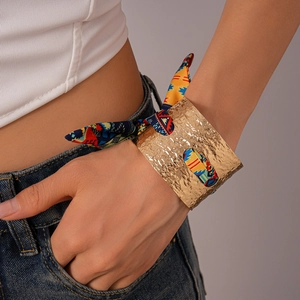 Dettaglio di bracciale rigido dorato martellato con nastro di seta etnico multicolore