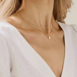 Close-up of double-layer gold chain necklace with white pearl pendant worn on neck