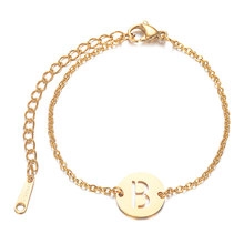 Close-up of golden stainless steel bracelet featuring a round disc with hollow letter B