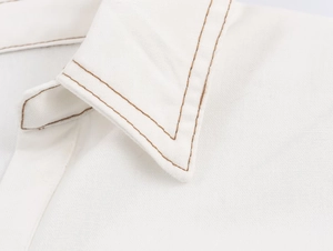 Vue détaillée du col blanc avec surpiqûres marron contrastées sur le tissu texturé