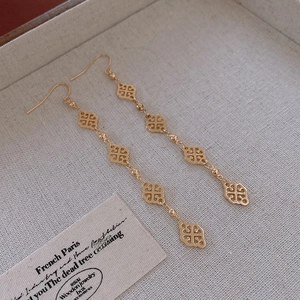Close-up of gold clover earrings on a beige linen tray with vintage tag detail