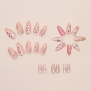Detail of almond-shaped press-on nails with golden cherry blossom motifs and fine glitter