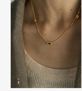 Close-up of vintage gold necklace with green zircon pendant on model wearing a suit