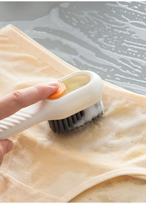 Close-up view of a white liquid-dispensing brush scrubbing soapy foam on soft cream fabric.