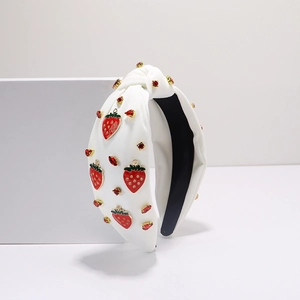 Détail du serre-tête noué en tissu blanc avec breloques fraises rouges et strass brillants
