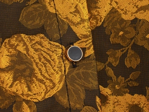Close-up of golden floral jacquard fabric and black round button on retro palace style dress