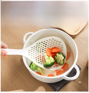 Detail of white long-handled plastic skimmer scooping broccoli and carrots from a pot