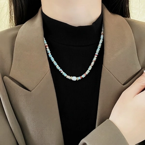 Colorful beaded pearl necklace with blue and red accents worn over a brown suit