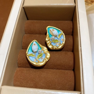Detail of gold-plated pearl flower earrings with blue enamel in a velvet jewelry box