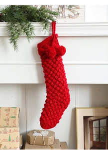 Detail of red cable knit Christmas stocking with pom poms hanging on a white fireplace