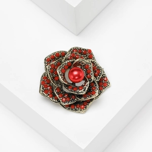 Macro view of rose-shaped brooch with red beads and central pearl on white stand