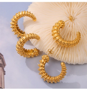 Macro detail of gold C-shaped earrings with beaded texture on white coral stone